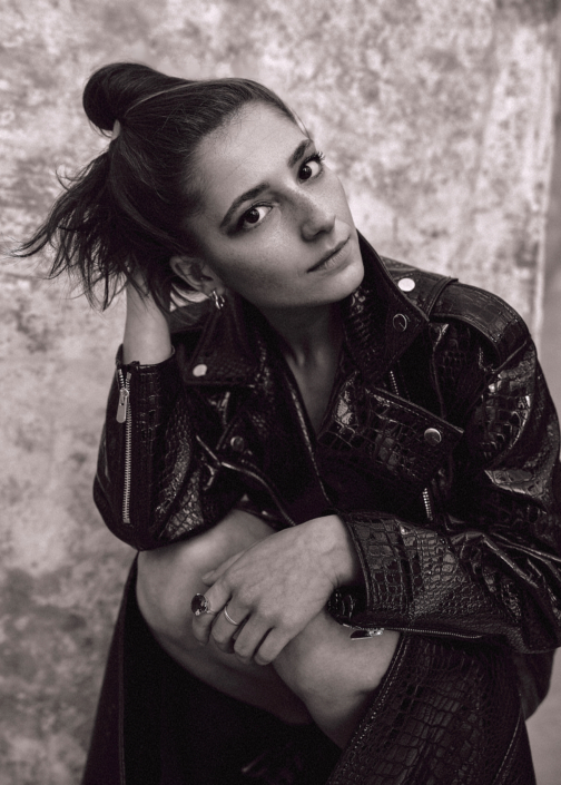 black and white Acting headshot of actress Elisha Applebaum wearing a leather jacket taken by photographer Kim Hardy in his London studio in front of a patchy background