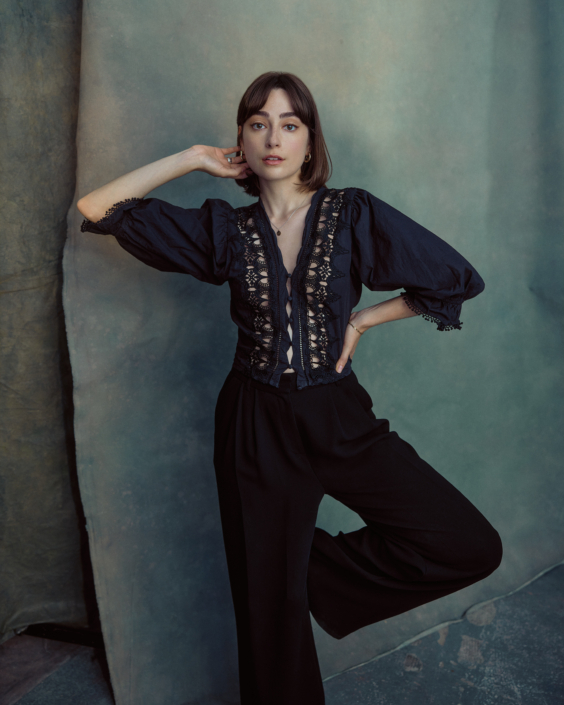 Acting headshot of Ellise Chappel wearing a lacy black top standing on one leg taken in the London studio of Kim Hardy in front of a blue-green background