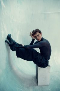 creative headshot of actor Joey Price, wearing high heels, leaning on his legs that are propped up on a textured background in a London studio taken by photographer Kim Hardy