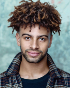 headshot of young black actor with curly hair taken by Kim Hardy in his London photography studio in front of a textured blueish background