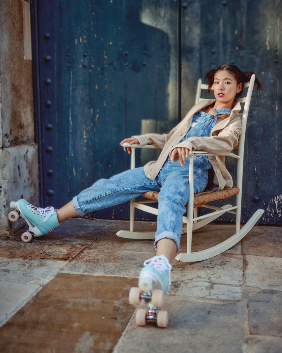 creative headshot of a young Asian woman sitting on a rocking chair wearing blue jeans and roller-skates taken on a London location by Kim Hardy