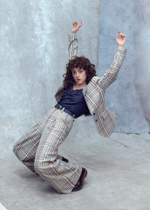 creative headshots of actor Eilidh Loan in a checked suit looking like she is falling over captured by photographer Kim Hardy in his London studio in front of a hand-painted cold backdrop