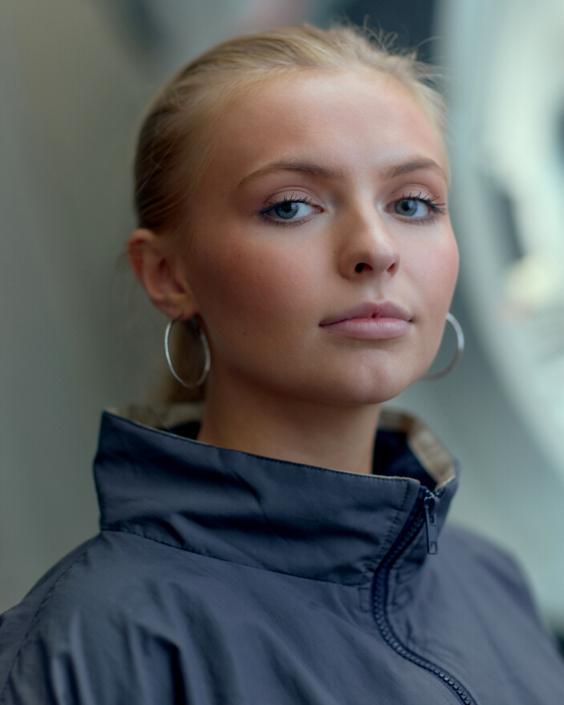 close up headshot of Lily Brunson young actress wearing hoop earrings and a hoodie in front of a blurred background taken by photographer Kim Hardy in his London studio